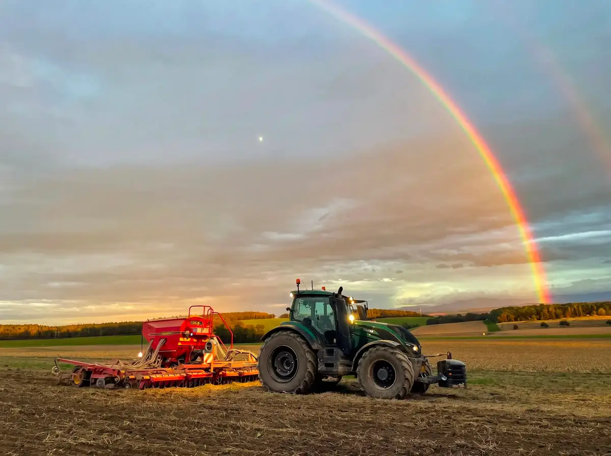 Traktor mit Drillmaschine bei der Aussaat unter einem Regenbogen